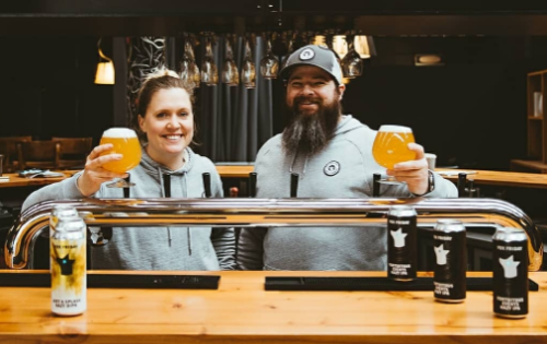 Picture of Benn and Sarah Hooper standing behind a bar holding glasses of beer
